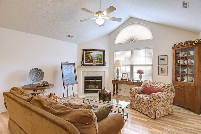 living room featuring light hardwood / wood-style floors, lofted ceiling, a tile fireplace, and ceiling fan