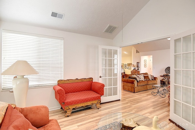 sitting room with lofted ceiling, hardwood / wood-style floors, a textured ceiling, and french doors