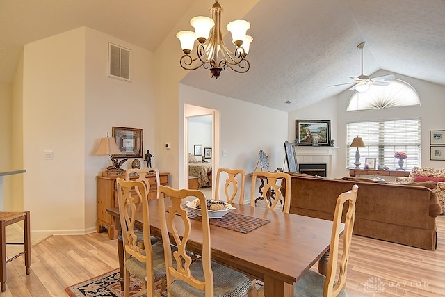 dining room featuring lofted ceiling, a tiled fireplace, a textured ceiling, light wood-type flooring, and ceiling fan with notable chandelier