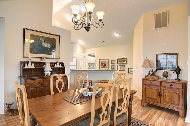 dining room featuring lofted ceiling, a chandelier, light hardwood / wood-style flooring, and a textured ceiling