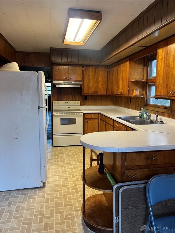 kitchen featuring a kitchen breakfast bar, kitchen peninsula, sink, white appliances, and wood walls