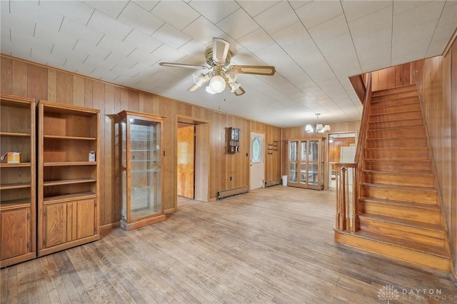 unfurnished living room featuring a baseboard radiator, wood-type flooring, ceiling fan with notable chandelier, and wood walls