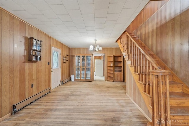 interior space featuring wooden walls, a notable chandelier, baseboard heating, and light hardwood / wood-style floors