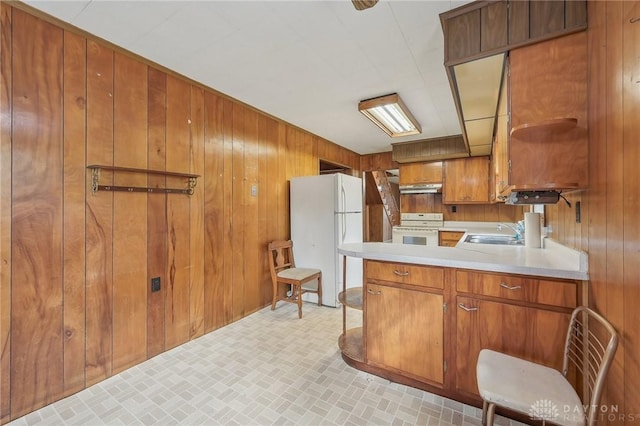 kitchen with white appliances, wooden walls, and sink