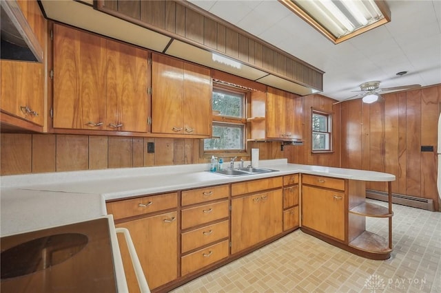 kitchen with sink, a baseboard radiator, wooden walls, kitchen peninsula, and ceiling fan