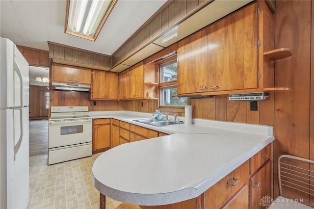 kitchen featuring sink, white appliances, kitchen peninsula, and wood walls