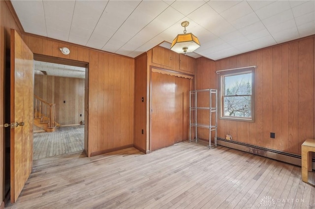 unfurnished bedroom featuring a baseboard radiator, wooden walls, a closet, and light hardwood / wood-style flooring