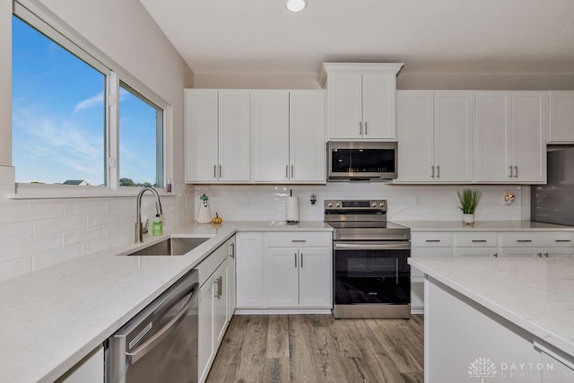 kitchen featuring decorative backsplash, sink, white cabinets, light wood-type flooring, and appliances with stainless steel finishes