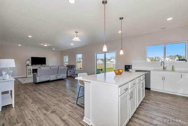 kitchen with white cabinets, a kitchen island, light hardwood / wood-style flooring, dishwasher, and pendant lighting