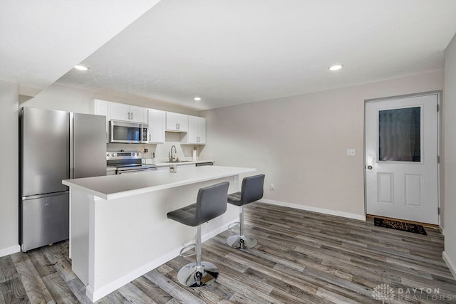 kitchen with a breakfast bar area, a center island with sink, hardwood / wood-style floors, white cabinets, and appliances with stainless steel finishes