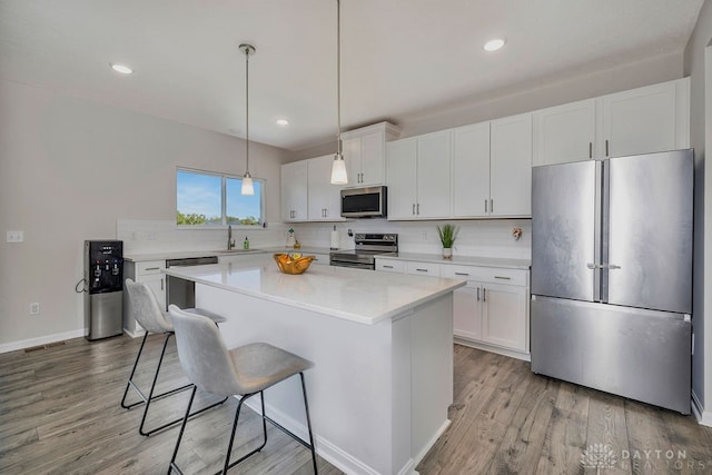 kitchen featuring white cabinets, light hardwood / wood-style flooring, sink, pendant lighting, and stainless steel appliances