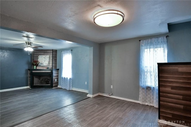 unfurnished living room featuring dark hardwood / wood-style flooring, ceiling fan, a textured ceiling, and a healthy amount of sunlight