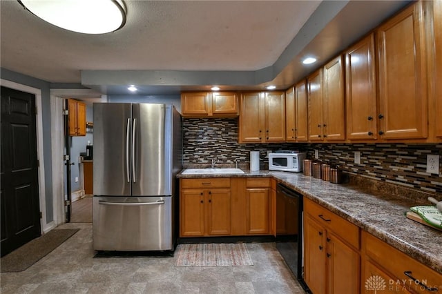 kitchen with sink, stainless steel fridge, black dishwasher, dark stone counters, and decorative backsplash