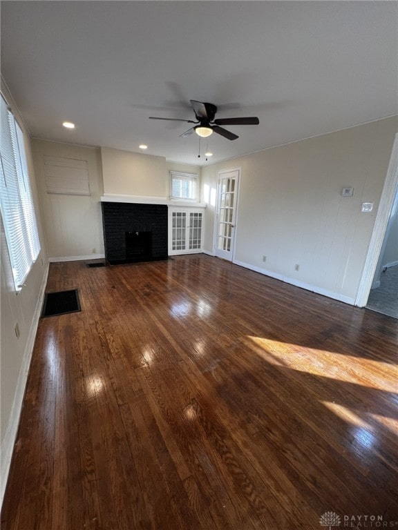 unfurnished living room with ceiling fan, a brick fireplace, and dark wood-type flooring