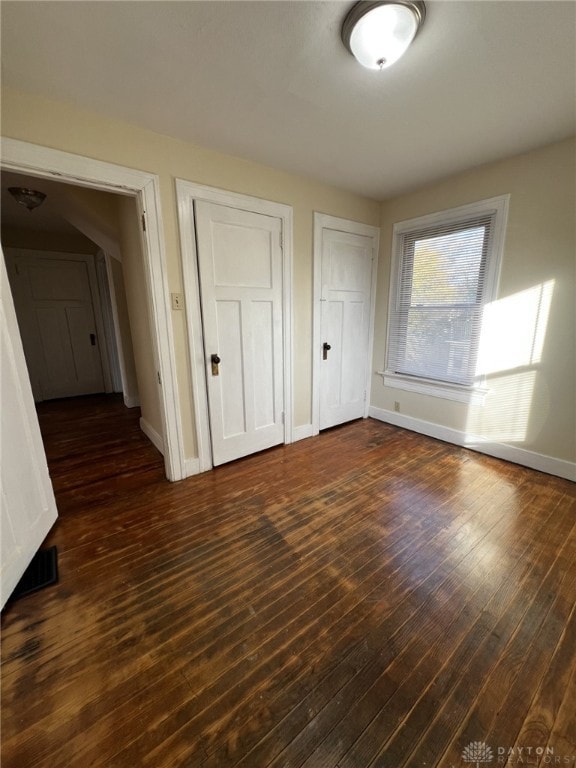 unfurnished bedroom with dark hardwood / wood-style floors and multiple closets