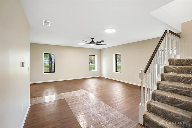 interior space featuring baseboards, visible vents, dark wood finished floors, a ceiling fan, and stairway