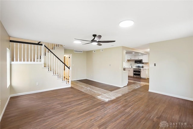 unfurnished living room featuring dark wood-style flooring, visible vents, a sink, and stairway