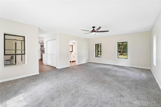 spare room with a ceiling fan, dark carpet, and baseboards