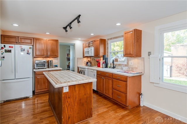 kitchen with tile counters, a center island, light wood-type flooring, plenty of natural light, and white appliances