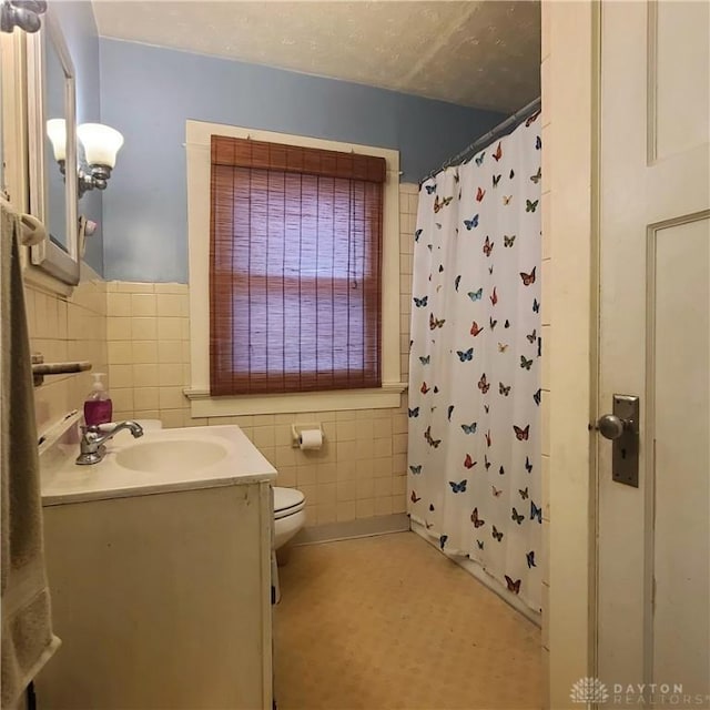 bathroom with a shower with curtain, vanity, toilet, and tile walls