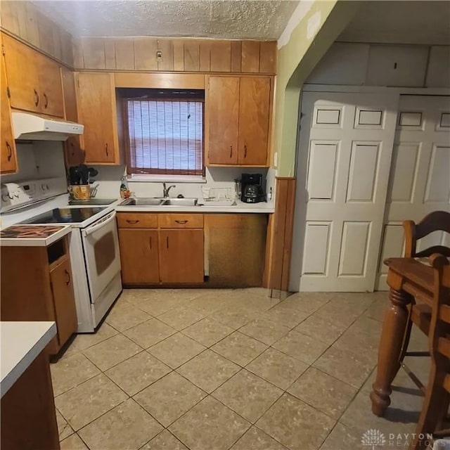 kitchen featuring light tile patterned flooring, a textured ceiling, white range with electric stovetop, and sink