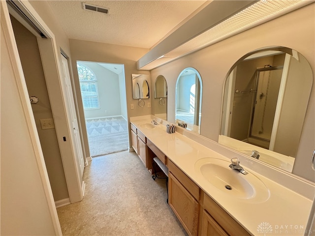 bathroom featuring visible vents, double vanity, a sink, a textured ceiling, and a shower with door