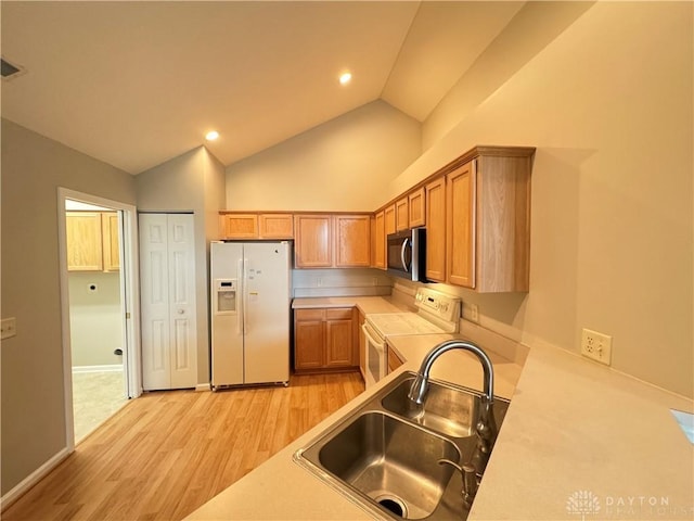 kitchen featuring light countertops, lofted ceiling, light wood-style flooring, white appliances, and a sink