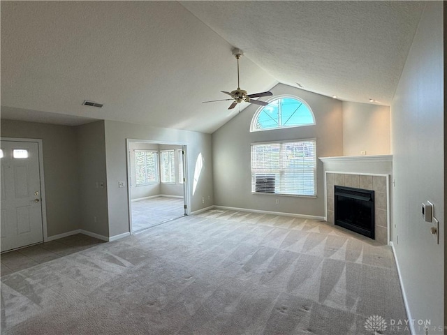 unfurnished living room with a tiled fireplace, visible vents, ceiling fan, and carpet floors