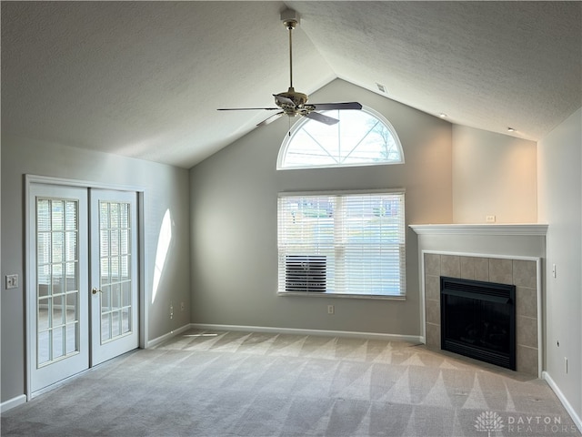 unfurnished living room featuring a textured ceiling, light colored carpet, lofted ceiling, a tile fireplace, and ceiling fan