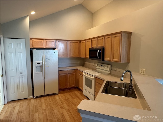 kitchen with light wood finished floors, light countertops, a peninsula, white appliances, and a sink