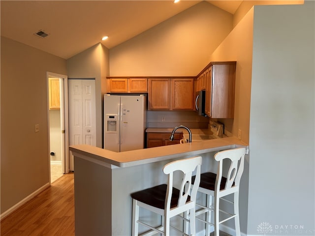 kitchen with light hardwood / wood-style floors, a breakfast bar, white fridge with ice dispenser, lofted ceiling, and stove