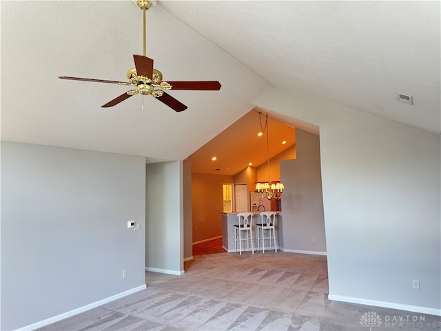 unfurnished living room featuring ceiling fan with notable chandelier, a textured ceiling, vaulted ceiling, and carpet