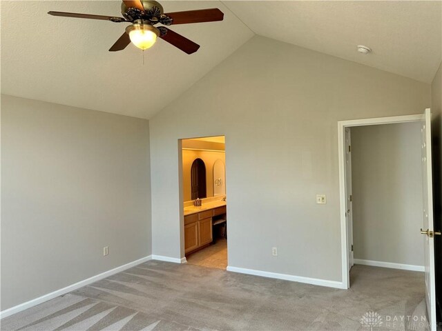 unfurnished bedroom with high vaulted ceiling, ensuite bath, baseboards, light colored carpet, and ceiling fan