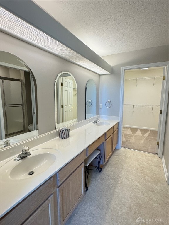 bathroom with a sink, an enclosed shower, a textured ceiling, and double vanity