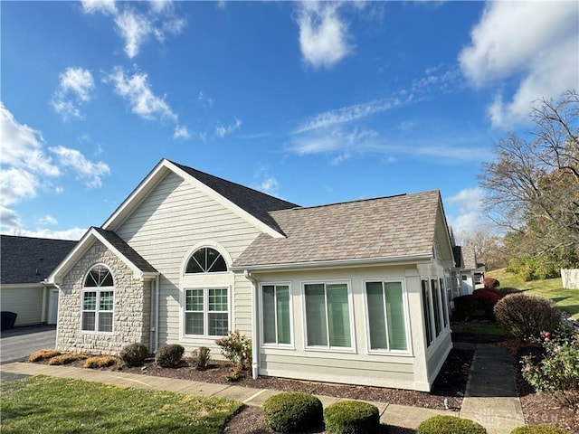 back of house with stone siding and roof with shingles