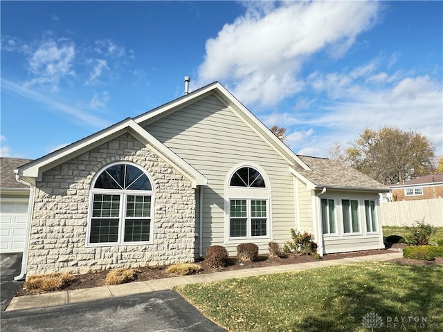 view of front facade featuring fence, an attached garage, a shingled roof, a front lawn, and stone siding