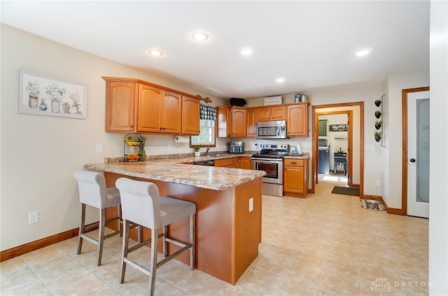 kitchen with sink, stainless steel appliances, kitchen peninsula, a breakfast bar area, and light tile patterned flooring