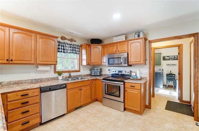 kitchen with light stone countertops, stainless steel appliances, washer / clothes dryer, and sink