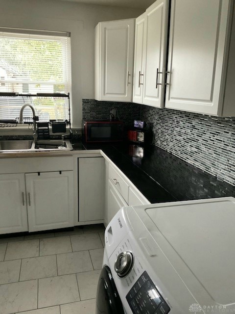 kitchen featuring washer / dryer, light tile patterned flooring, sink, backsplash, and white cabinetry