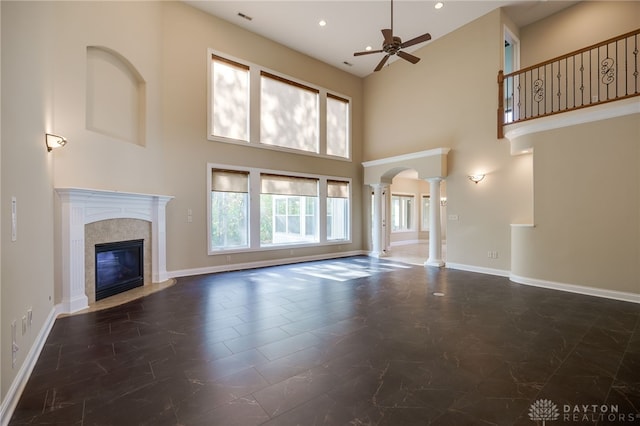 unfurnished living room featuring decorative columns, a tiled fireplace, a towering ceiling, and a wealth of natural light