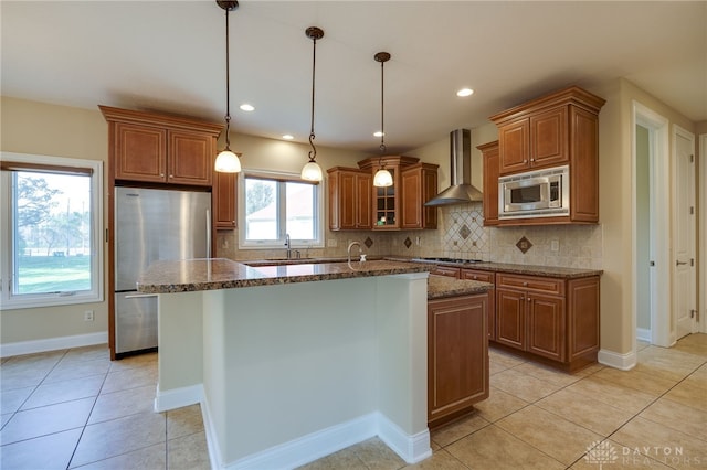 kitchen with wall chimney exhaust hood, a healthy amount of sunlight, dark stone countertops, a center island with sink, and appliances with stainless steel finishes