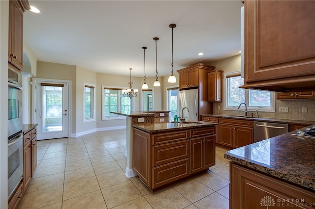 kitchen with decorative backsplash, a kitchen island with sink, stainless steel appliances, decorative light fixtures, and plenty of natural light