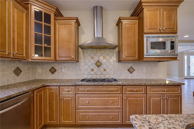 kitchen with wall chimney range hood, stainless steel appliances, light stone counters, and backsplash