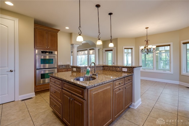 kitchen featuring an island with sink, decorative columns, sink, double oven, and decorative light fixtures