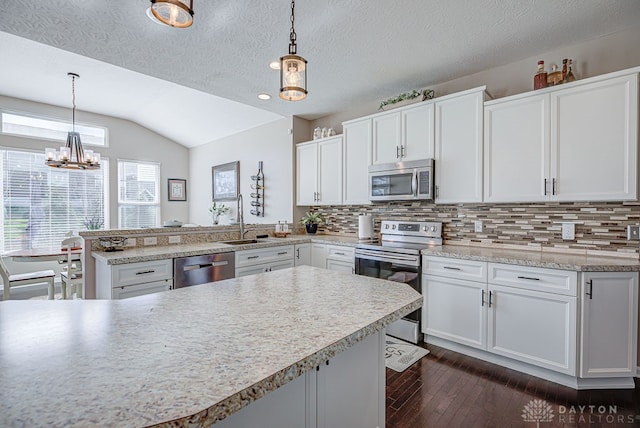 kitchen with white cabinetry, sink, appliances with stainless steel finishes, hanging light fixtures, and lofted ceiling