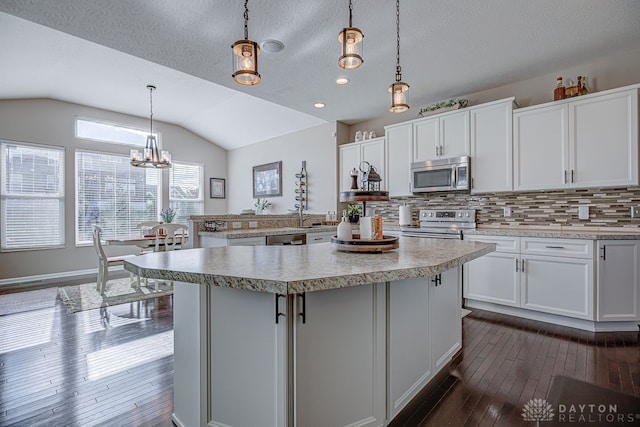 kitchen with stainless steel appliances, white cabinetry, decorative light fixtures, lofted ceiling, and a center island