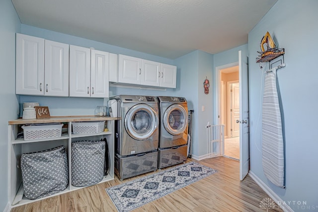 washroom featuring washing machine and clothes dryer, cabinets, a textured ceiling, and light hardwood / wood-style flooring