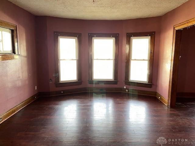 spare room with a textured ceiling, dark wood-type flooring, and a healthy amount of sunlight