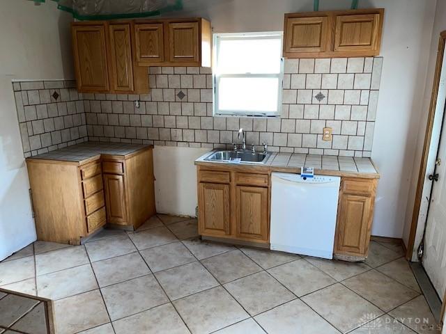 kitchen featuring sink, white dishwasher, tasteful backsplash, tile counters, and light tile patterned flooring