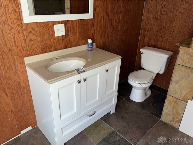 bathroom featuring vanity, toilet, and wood walls